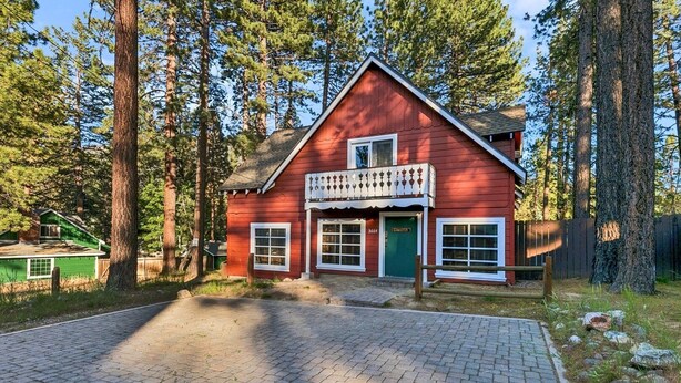 A red wooden house with a balcony, surrounded by tall trees.