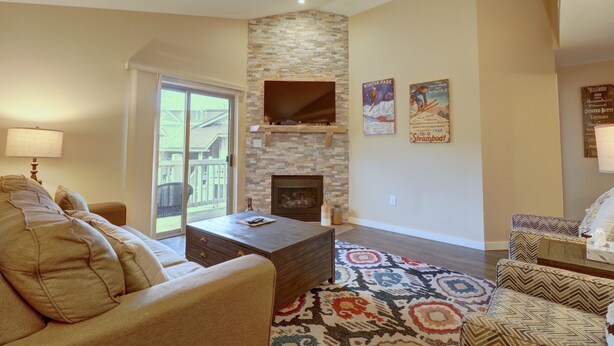 A living room with a stone fireplace, a sofa, a coffee table, and a patterned rug. - 201 Point Drive 2 Bedroom Condo by RedAwning (Frisco)