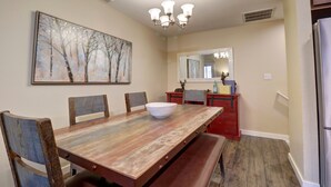 A dining room with a wooden table, chairs, a large painting, a chandelier, and a refrigerator. - 201 Point Drive 2 Bedroom Condo by RedAwning (Frisco)