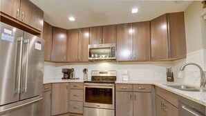 A modern kitchen with stainless steel appliances, wooden cabinets, and a granite countertop. - 201 Point Drive 2 Bedroom Condo by RedAwning (Frisco)
