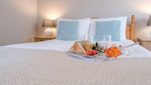 Ein ordentlich bezogenes Bett mit einem Frühstücksbrett, das Toast, Erdbeeren und eine Rose enthält.
