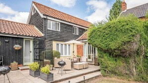Ein zweistöckiges Haus mit einem Ziegeldach, einer Terrasse mit Gartenmöbeln und einem Garten.