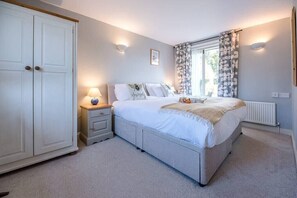 Cozy retreat with a large bed, wardrobe, and nightstand, featuring a window with curtains and a radiator.