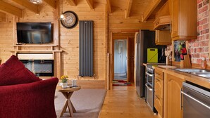 A wooden interior with a TV, fireplace, kitchen, and a red chair.