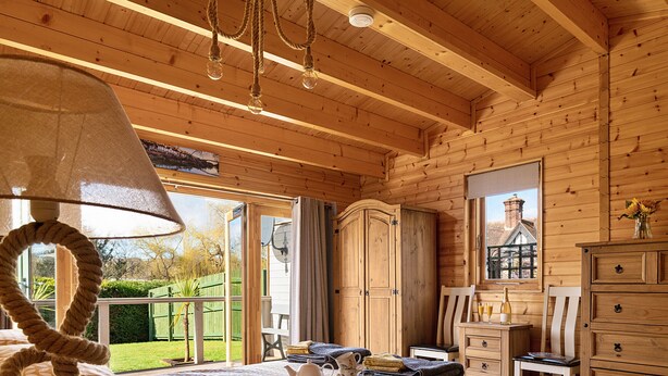 A wooden cabin bedroom with a bed, a dresser, a chair, and a table with breakfast items.