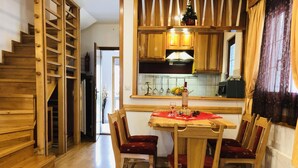 A wooden staircase leading to a dining area with a table set for two, chairs, and a kitchen in the background. - Kraljevi Konaci Zlatibor (Zlatibor)