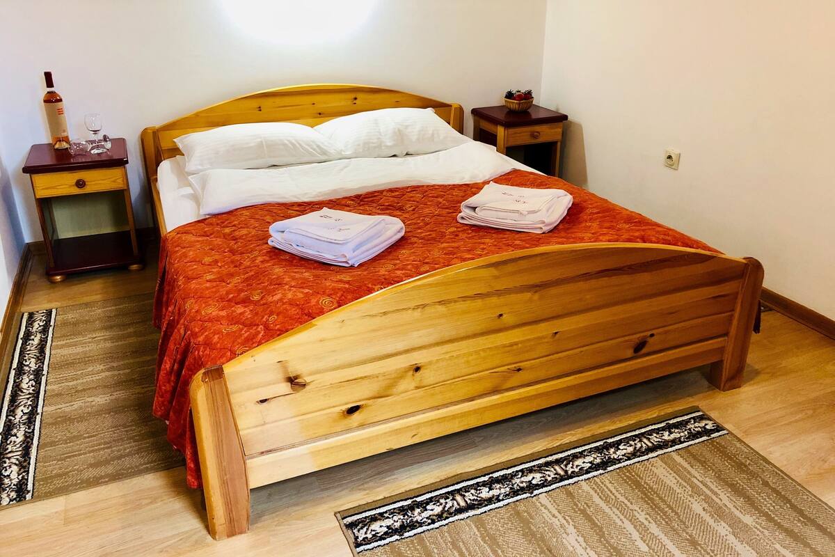 Un lit bien fait, avec une couvre-lit rouge, une tête de lit en bois et deux tables de chevet dotées de tiroirs.