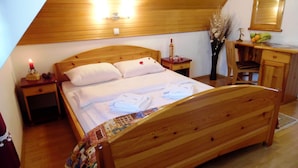A wooden-framed bed in a room with a sloped ceiling, a nightstand with a candle, and a mirror above a dresser. - Kraljevi Konaci Zlatibor (Zlatibor)