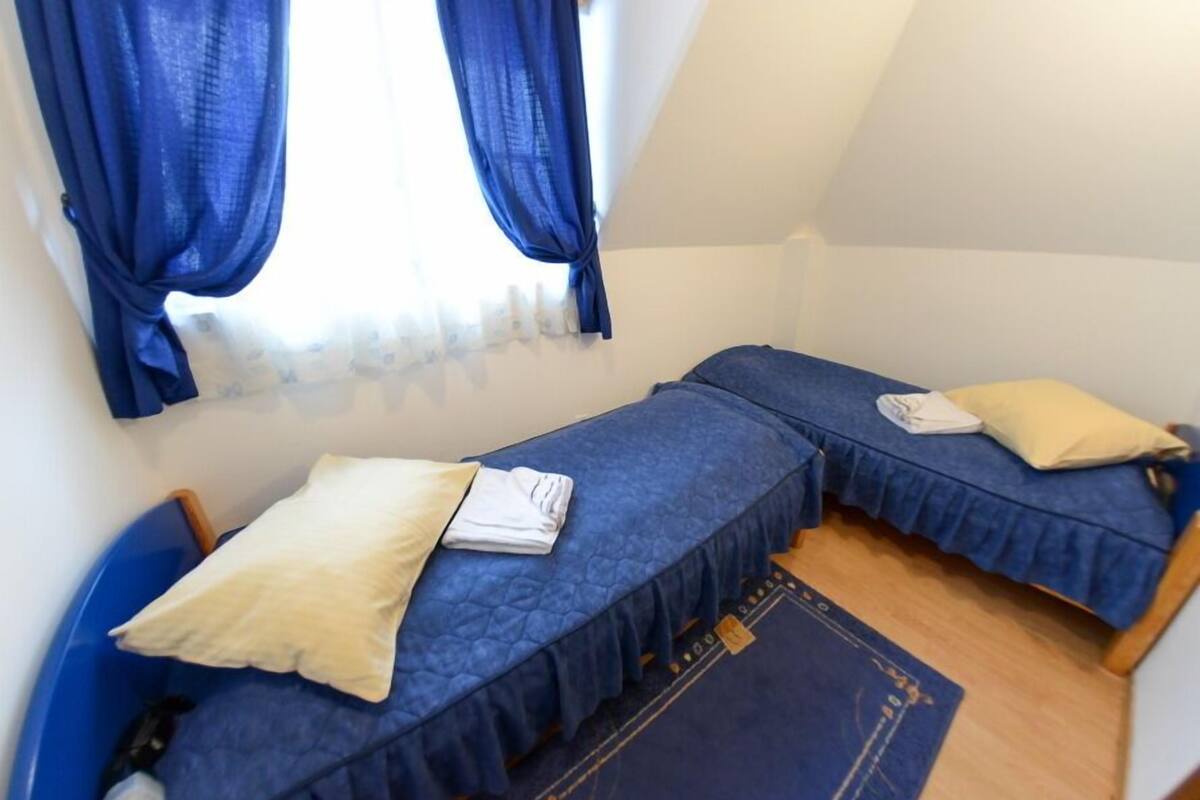 Un petit logement composé d’une seule pièce, avec deux lits, chacun recouvert d’une couverture bleue et doté d’un oreiller.