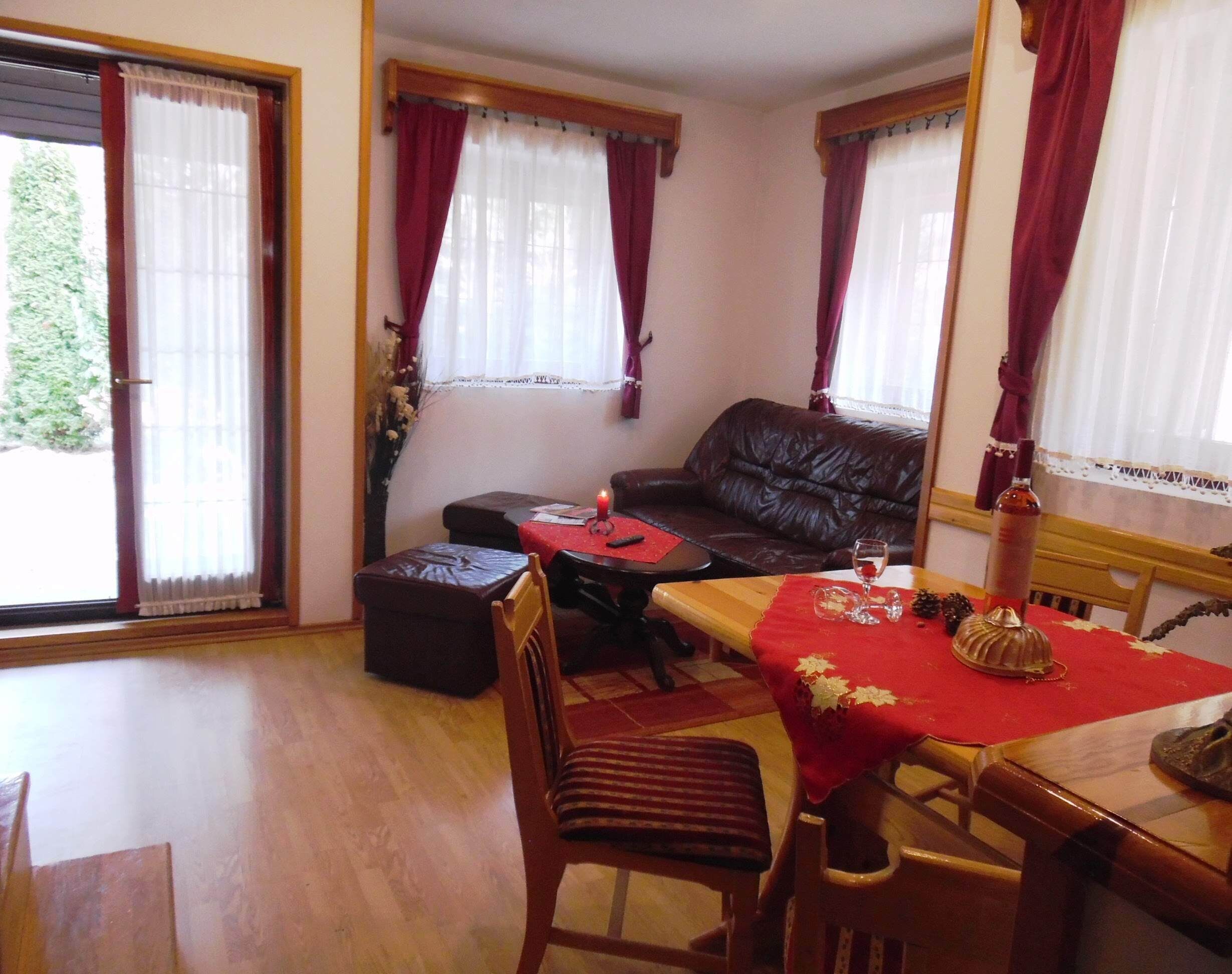 A cozy living room with a leather sofa, a dining table with a red tablecloth, and a fireplace.
