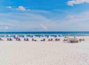 A beach with rows of sun loungers and umbrellas, a flag, and the ocean in the background. - Beachfront Condo with Spectacular Views and Heated Pool! (Orange Beach)