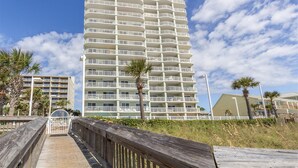 A tall, multi-story hotel with balconies, located near a beach with a wooden boardwalk. - Beachfront Condo with Spectacular Views and Heated Pool! (Orange Beach)