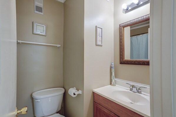 Ein Badezimmer mit Toilette, Waschbecken, Waschtisch, Spiegel, Handtuchhalter und einem gerahmten Bild an der Wand.