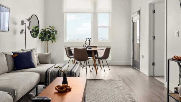 A modern living room with a sofa, a coffee table, and a dining area with chairs and a table. - City Views | Lifestyle Loft | Zuni Lofts (Denver)
