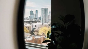 A view through a window of a cityscape with tall buildings and a plant in the foreground. - City Views | Lifestyle Loft | Zuni Lofts (Denver)