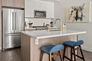 Una cocina moderna con electrodomésticos de acero inoxidable, una isla con cubierta blanca y taburetes de bar.