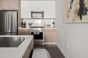 A modern kitchen with stainless steel appliances, wooden cabinets, and a minimalist design. - City Views | Lifestyle Loft | Zuni Lofts (Denver)