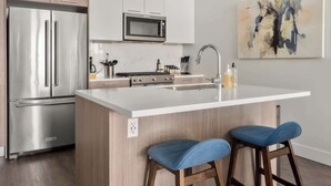 A modern kitchen with stainless steel appliances, a white countertop, and a bar stool. - City Views | Lifestyle Loft | Zuni Lofts (Denver)