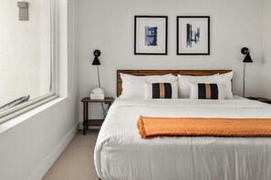 A hotel room with a large bed, two bedside tables, a window, and two framed artworks on the wall. - City Views | Lifestyle Loft | Zuni Lofts (Denver)