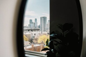 A view through a window with a cityscape in the background, including high-rise buildings and a plant in the foreground. - City Views | Lifestyle Loft | Zuni Lofts (Denver)