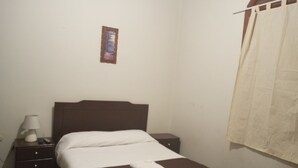 A bedroom with a bed, a nightstand, a lamp, a framed picture on the wall, and a window with a curtain. - EL MONARCA AREQUIPA (Arequipa)