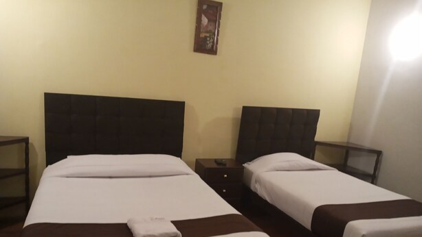 A hotel room with two beds, each with a dark headboard and white bedding. There is a small table and a nightstand with a lamp on each side of the beds. - EL MONARCA AREQUIPA (Arequipa)