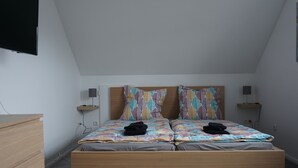 Ein Schlafzimmer mit einem hölzernen Bett, zwei Kissen, einem Nachttisch, einem an der Wand montierten Fernseher und einem Lautsprecher.