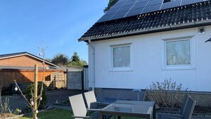 Ein Haus mit Solaranlage auf dem Dach, einem eingezäunten Garten und einem Tisch mit Stühlen.
