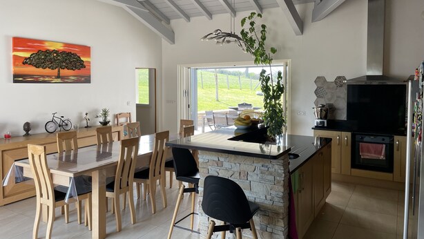 Une cuisine moderne dotée d’un îlot central en pierre, d’un ensemble de salle à manger en bois et d’une grande fenêtre offrant une vue sur l’extérieur.