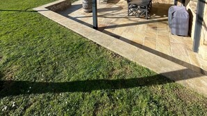 Un patio couvert avec un sol en pierre, des meubles d’extérieur et un bâtiment en pierre surmonté d’un toit rouge.