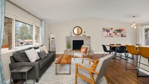 A modern living room with a sofa, coffee table, and chairs, a dining area with a table and chairs, a TV, and a fireplace.