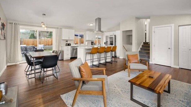 A modern kitchen with white cabinets, a central island with bar stools, and a dining area with a wooden table and chairs.