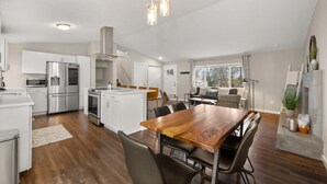 A modern kitchen with stainless steel appliances, a wooden dining table, and a large window providing natural light.