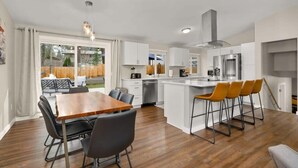 A modern kitchen with white cabinets, a central island with bar stools, and a dining area with a wooden table and chairs.