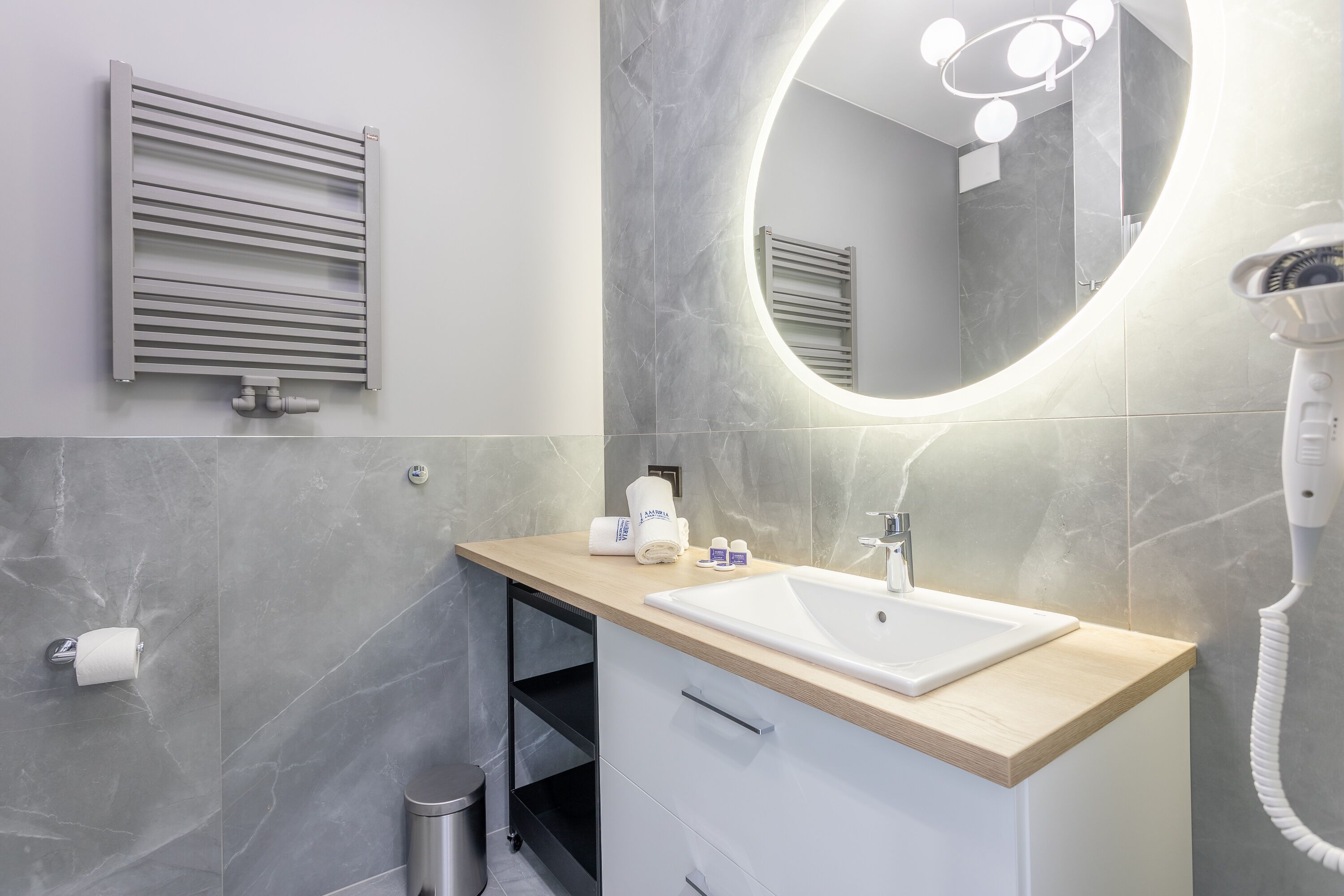 Une salle de bain moderne dotée d’un lavabo intégré, d’un miroir avec éclairage intégré, d’un porte-serviettes et d’un sèche-cheveux.