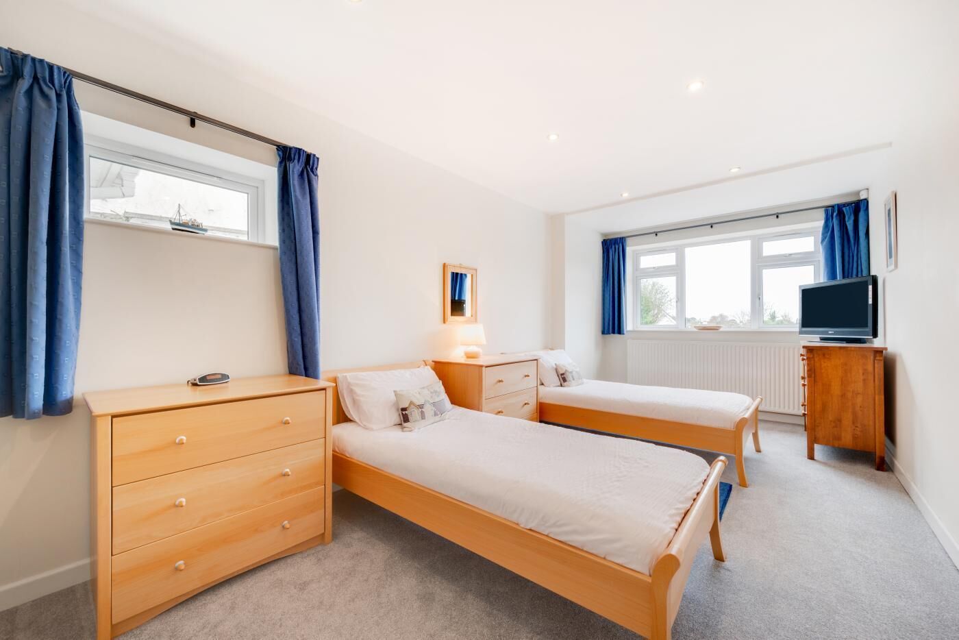 A bedroom with two single beds, a wooden dresser, a TV stand, and a window with curtains.