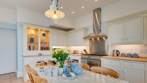 A modern kitchen with white cabinetry, a central island with seating, a stainless steel range hood, and a pendant light. - 5 Bed in Torquay (oc-bcvane) (Torquay)