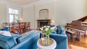 A living room with a grand piano, a dining area with wooden chairs, and a fireplace. - 5 Bed in Torquay (oc-bcvane) (Torquay)
