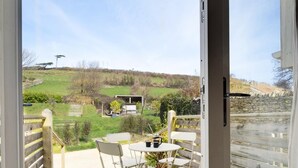 An open door to a balcony with a view of a grassy landscape, a table with chairs, and a small structure in the background. - 3 Bed in Croyde (oc-croyco) (Braunton)