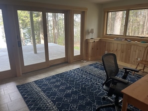 A room with a large sliding glass door leading to a deck, a wooden desk, a chair, and a blue patterned rug.