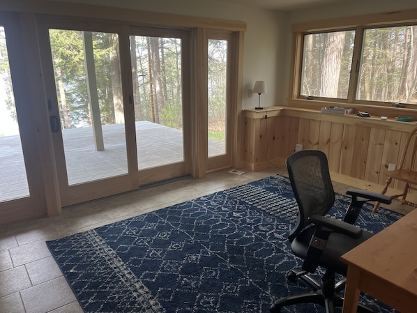 A room with a large sliding glass door leading to a deck, a wooden desk, a chair, and a blue patterned rug.