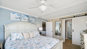 Un dormitorio con una cama grande, ventilador de techo y obras de arte en las paredes.