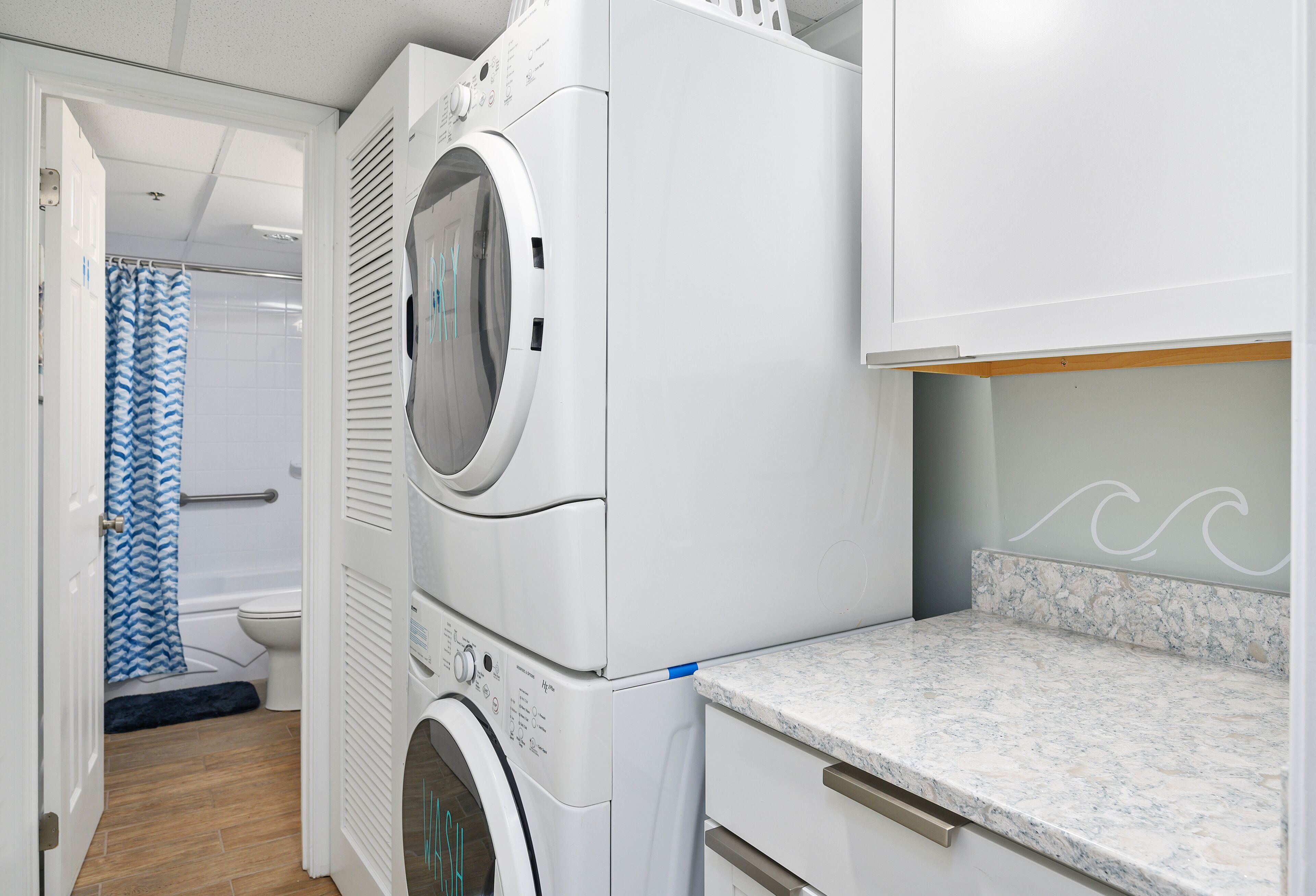 A laundry area with a front-loading washer and dryer, a bathroom with a shower curtain, and a marble countertop.