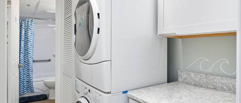 A laundry area with a front-loading washer and dryer, a bathroom with a shower curtain, and a marble countertop.