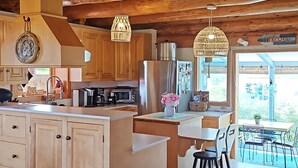 A spacious kitchen with wooden cabinetry, a large island, and a view of the outdoors. - 5 Star Log Beach House by the Ocean (Saint Peters Bay)