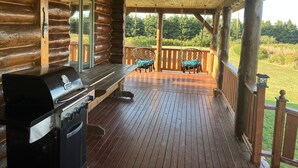 A wooden deck with a grill, two chairs, and a view of the outdoors. - 5 Star Log Beach House by the Ocean (Saint Peters Bay)