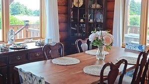 A wooden dining room with a chandelier, a wooden cabinet with glass doors, and a view of greenery outside. - 5 Star Log Beach House by the Ocean (Saint Peters Bay)