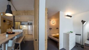 Une cuisine moderne agrémentée de touches de bois, un coin repas avec une table et des chaises, et une chambre confortable avec un lit et une lampe de chevet.