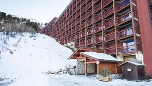 Un hôtel à plusieurs étages, doté de balcons, d’une entrée en pierre et, en arrière-plan, d’une pente enneigée.
