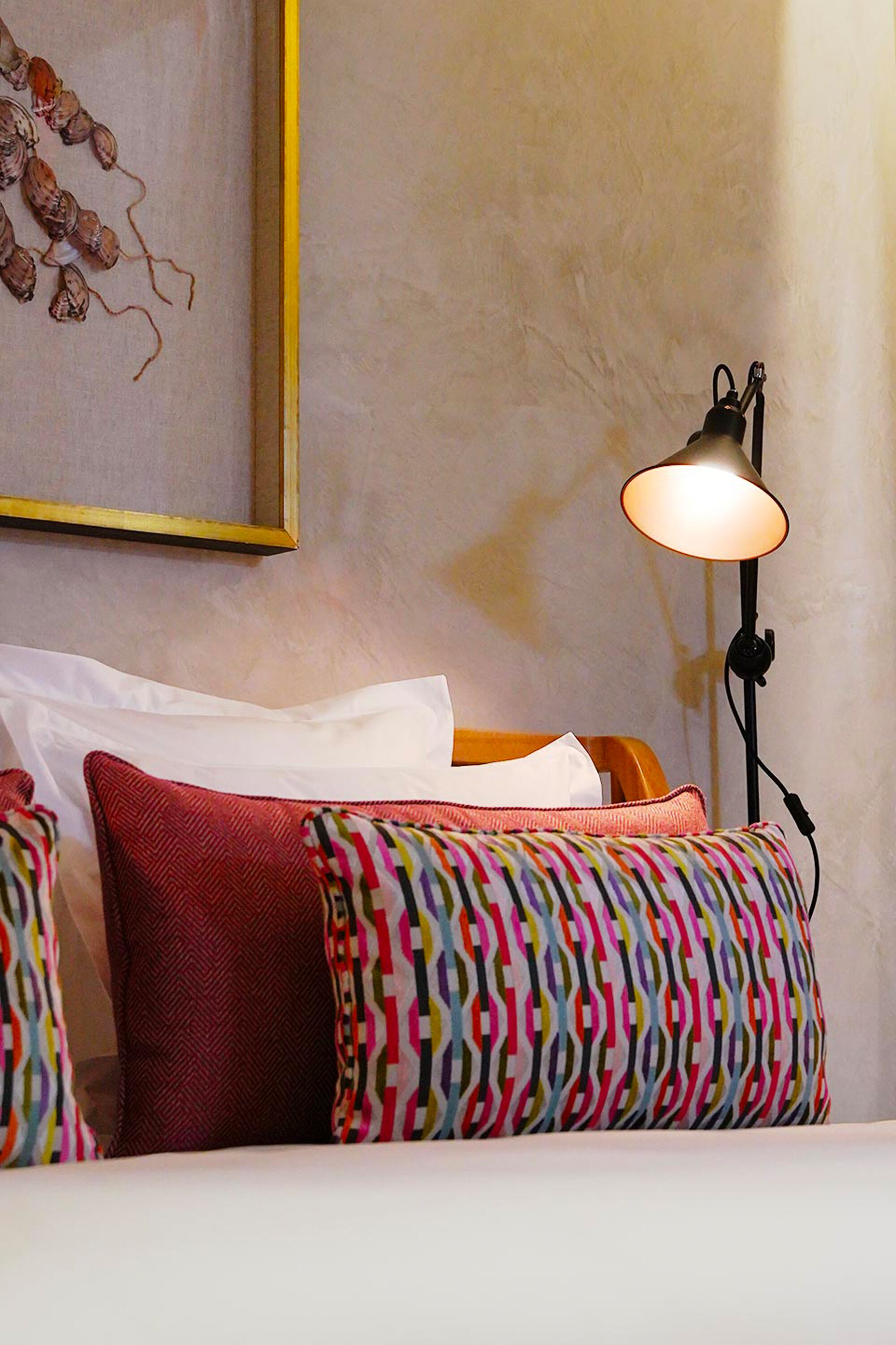 A neatly made bed with colorful pillows, a lamp on a bedside table, and a framed artwork on the wall.